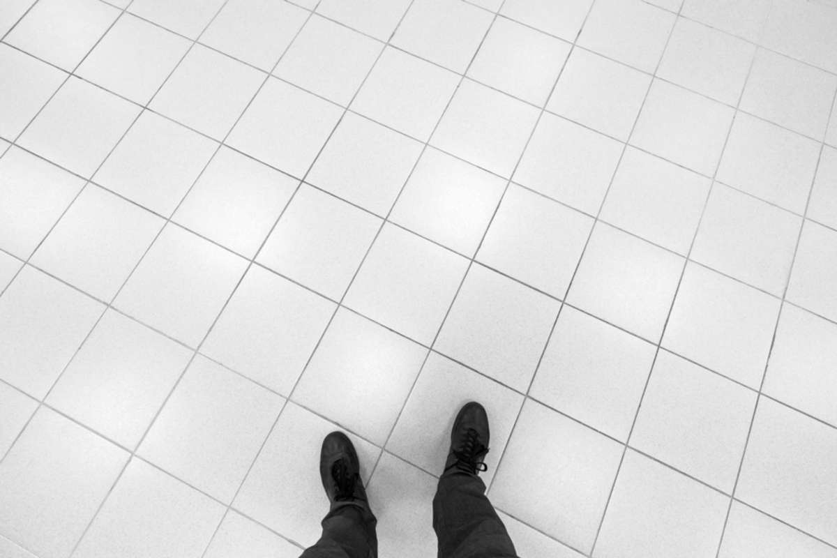 Male feet stand on office floor with white shining square tiling